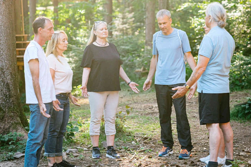 Eine therapiegruppe steht drau&szlig;en in der natur im kreis mit offenen h&auml;nden